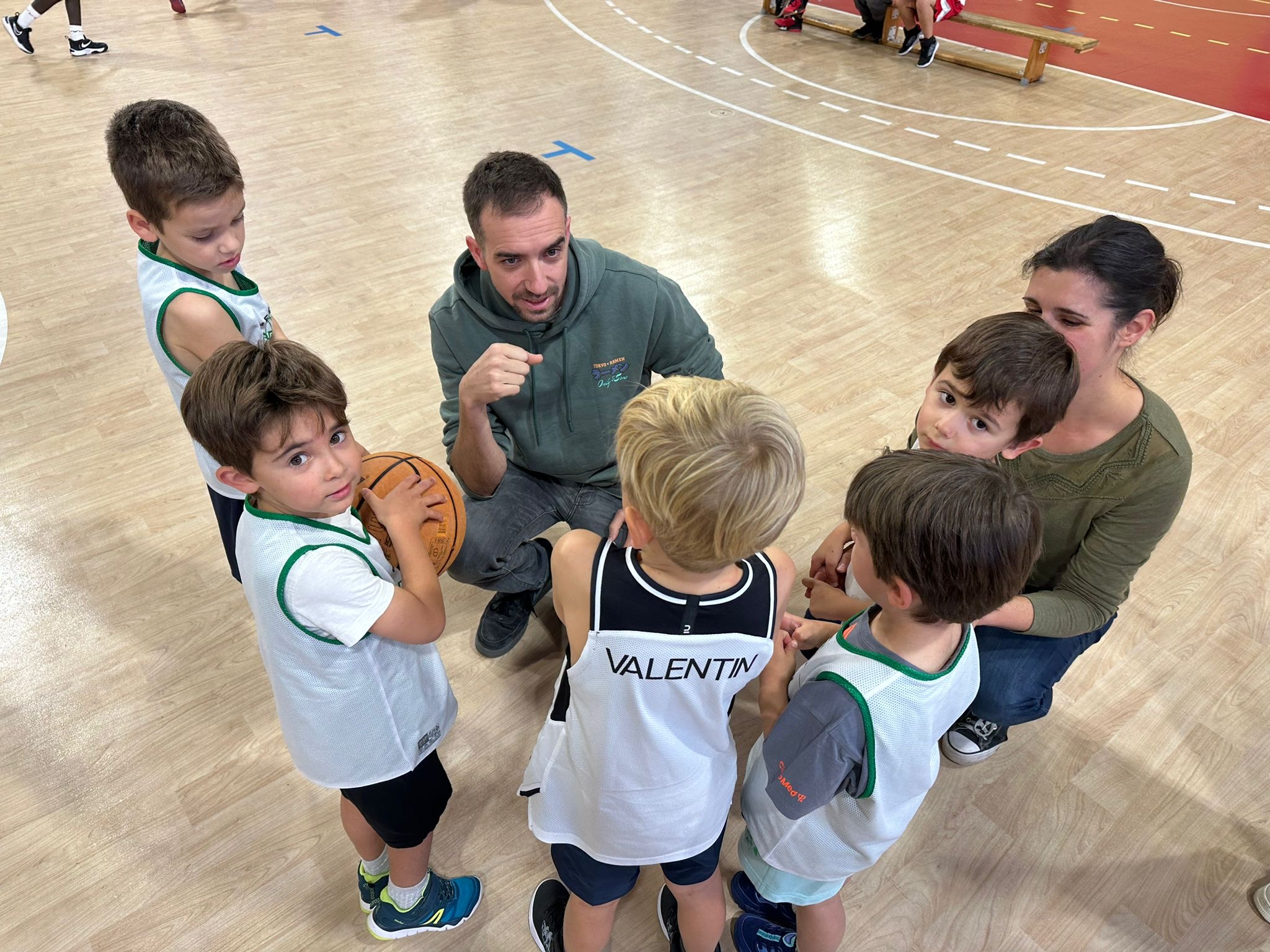 Un coach de l'ESEMT entouré des enfants du baby basket, ballon en main