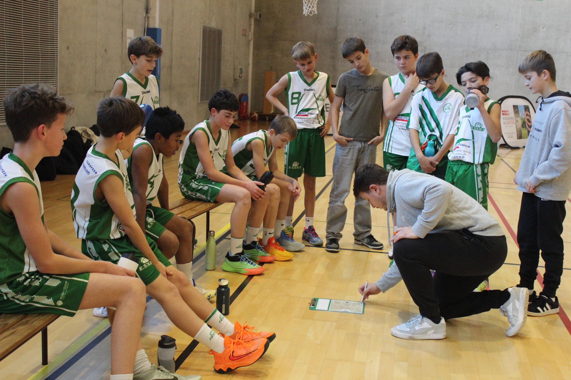 Un coach dessine un schéma sur sa tablette devant les jeunes joueurs de l'ESEMT